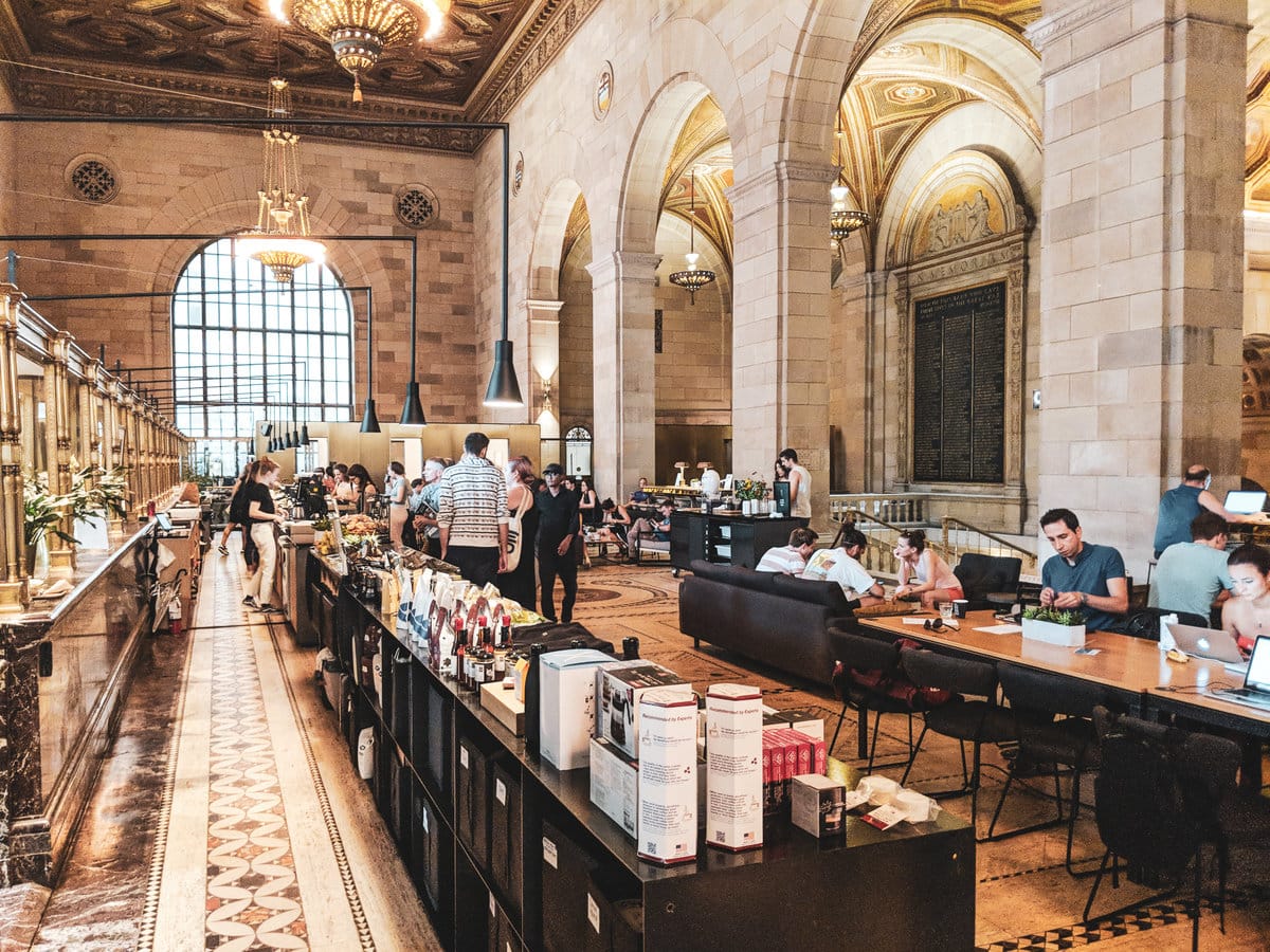 A spacious yet vibrant café reminiscent of a castle with high ceilings and old-fashioned decor, contrasted by modern black furnishings.