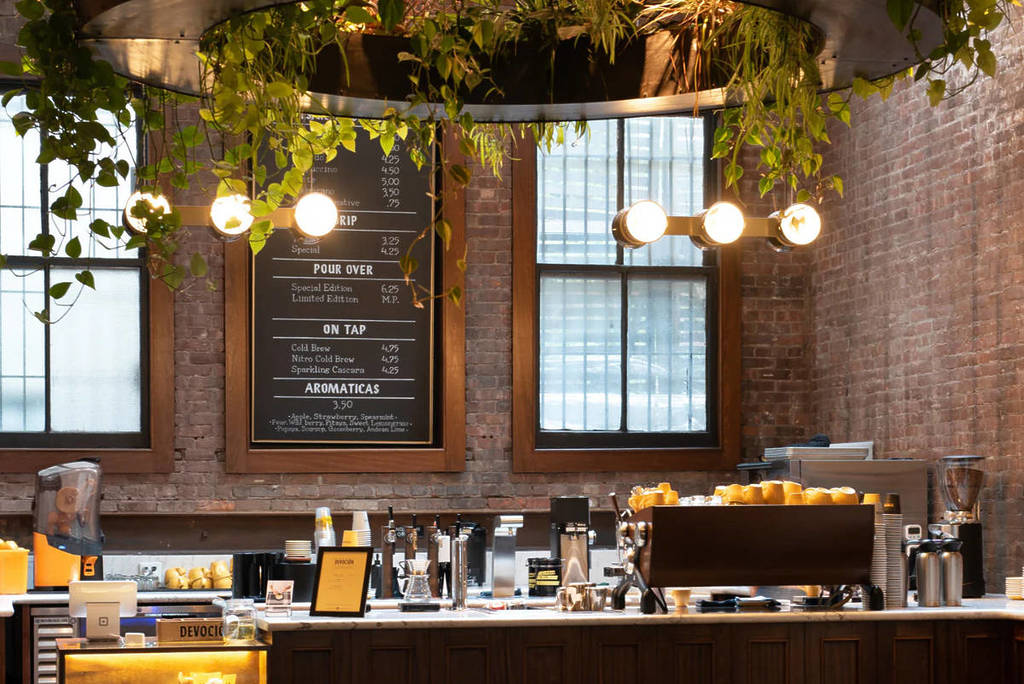 A well lit, modern café with brick walls and lush greenery cascading from the ceiling.