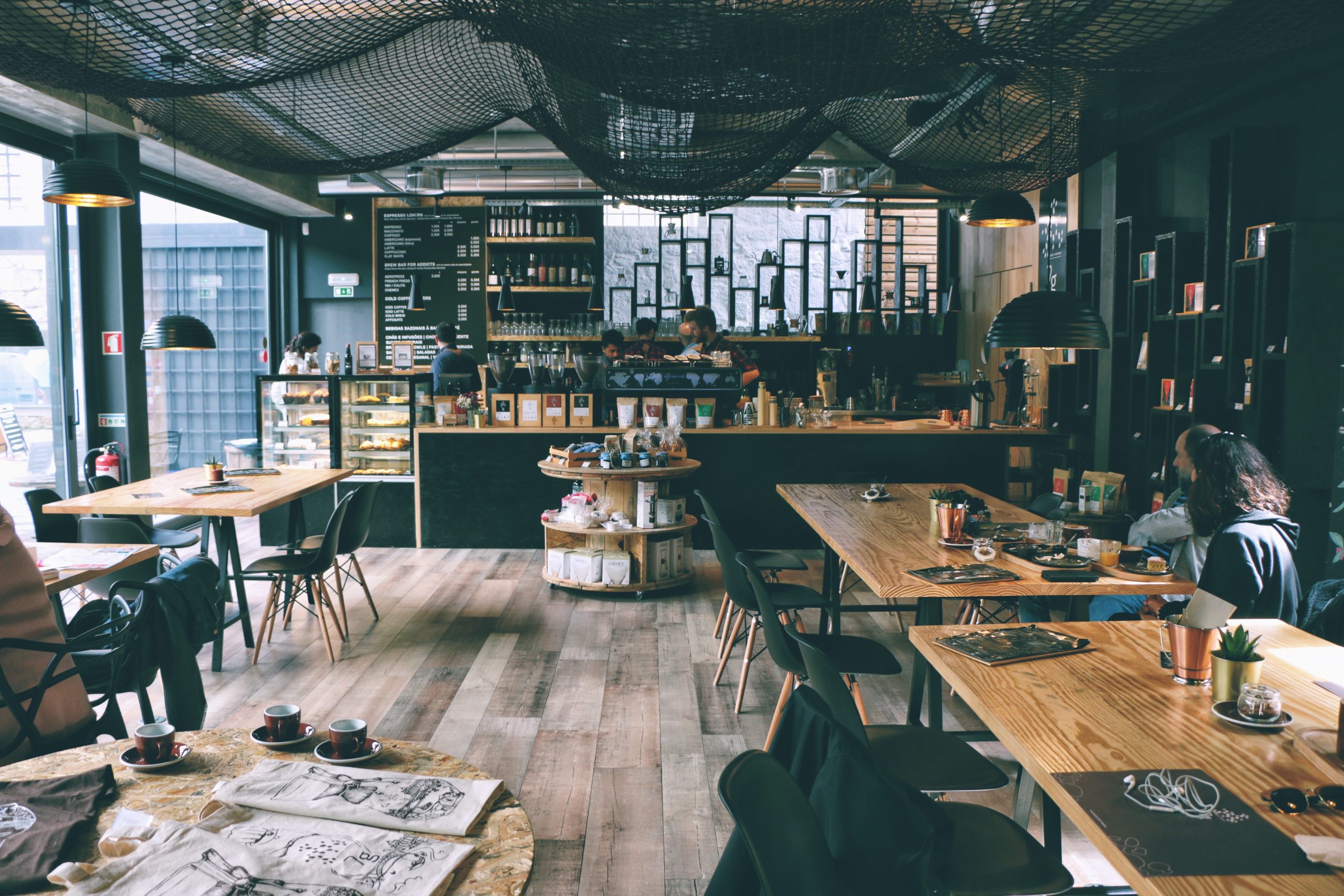 A spacious, light-filled café with dark walls, wooden décor, and distinctive black netting hanging from the ceiling.