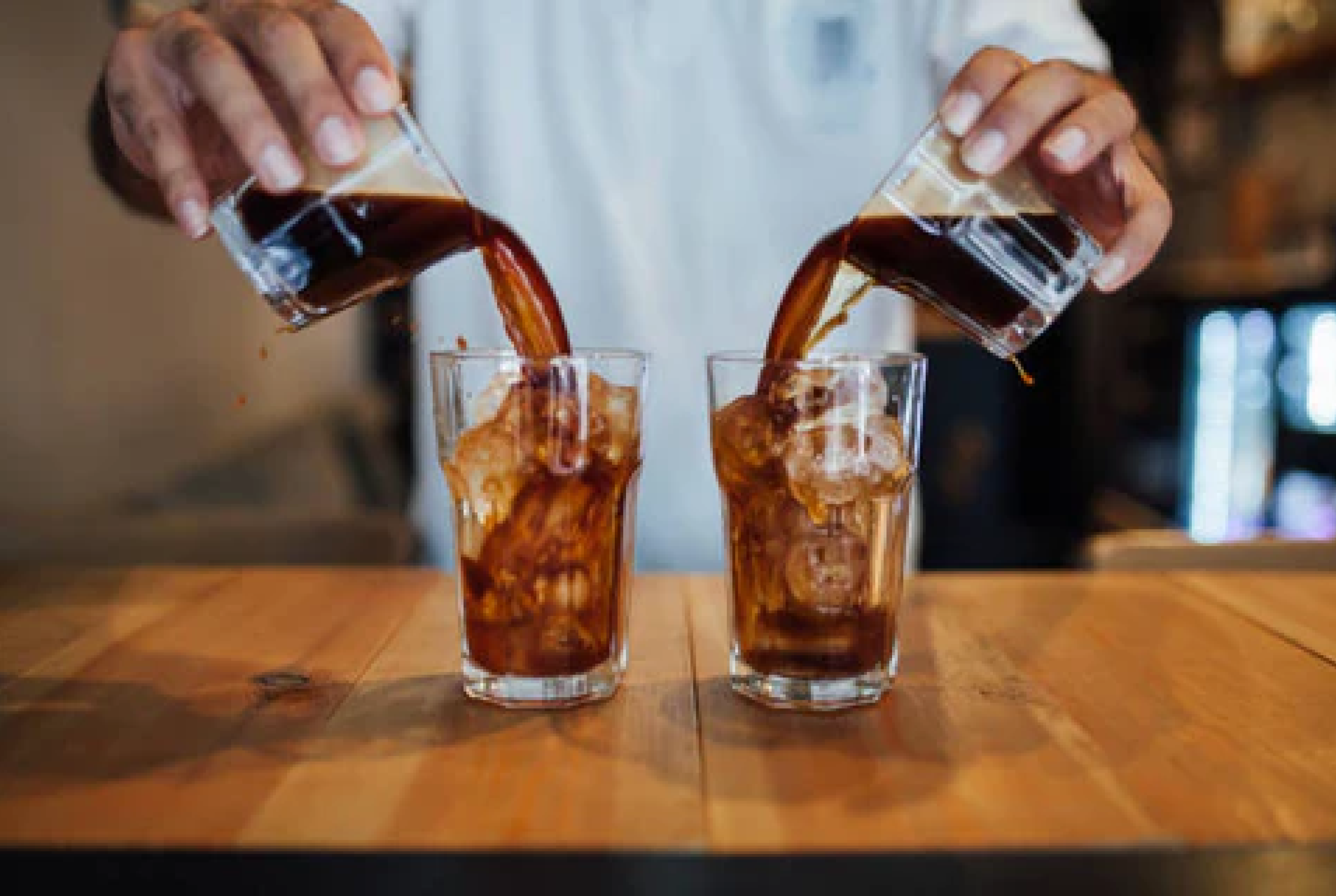 A picture of a person pouring coffee from two glasses to two new ones with ice