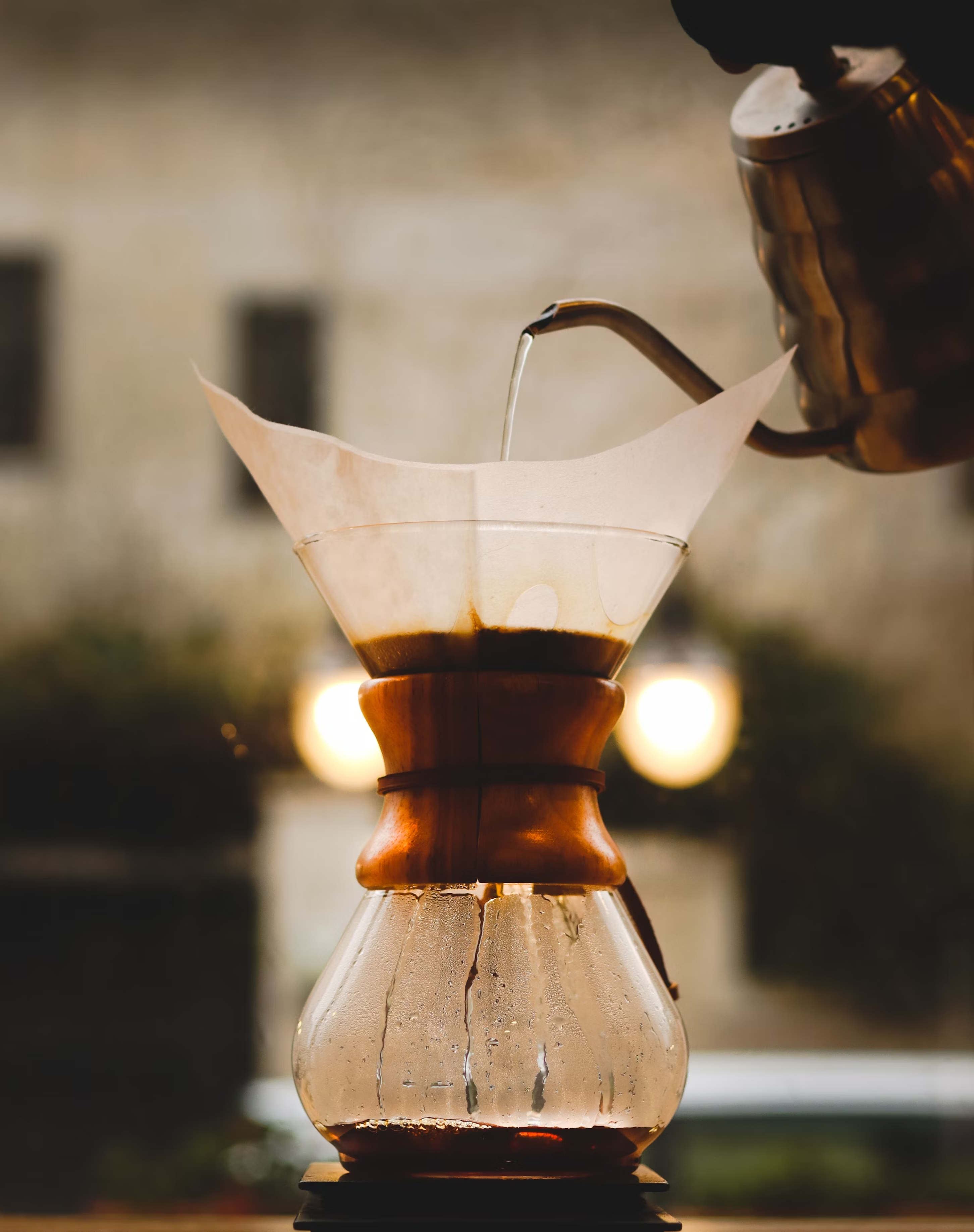 A picture of an older coffee pot pouring hot water to a pot with a filter with coffee on