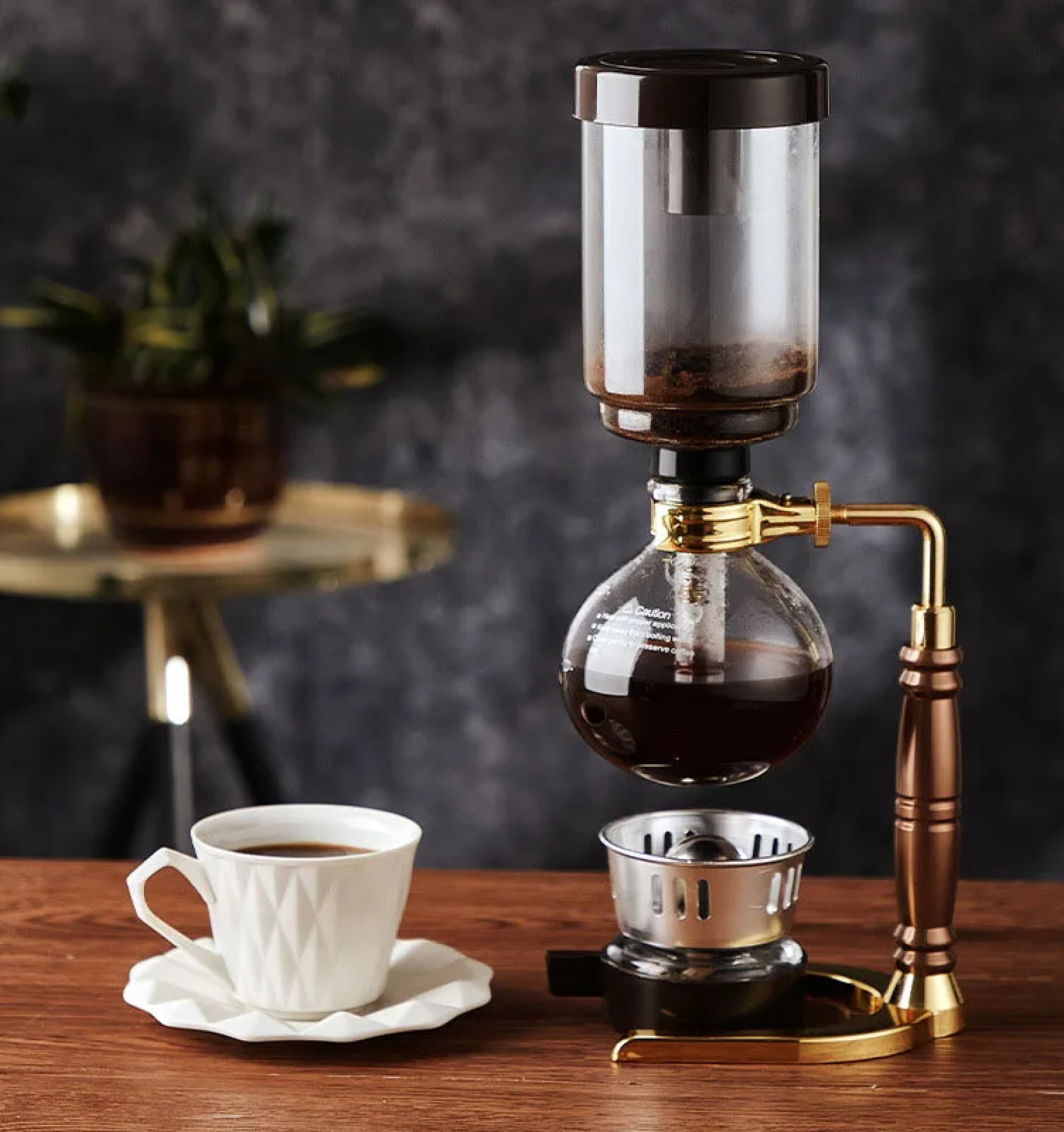 A picture of a siphon coffeemaker and and white little coffee cup